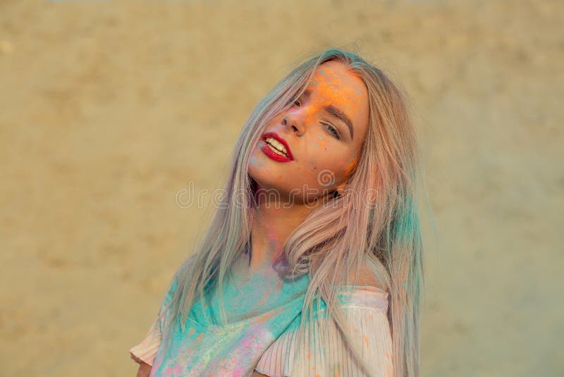 Closeup portrait of fashionable blonde model with red lips playing with orange dry paint Holi at the desert. Closeup portrait of fashionable blonde woman with stock photo